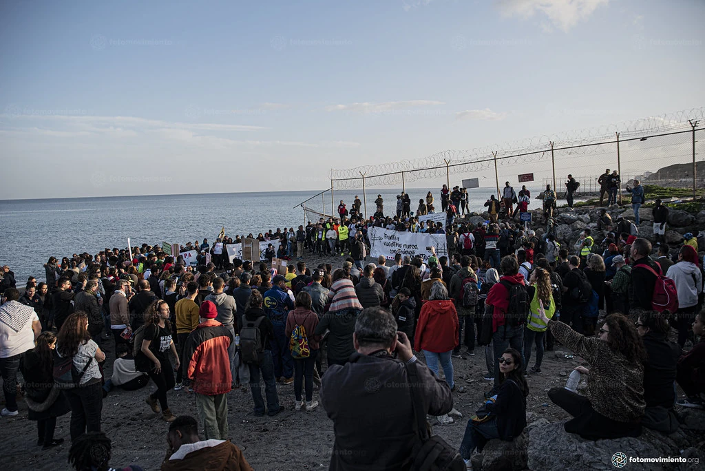 Concentración de personas con pancartas junto al mar y la valla de Ceuta